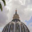 The dome of St. Peter’s Basilica rising against a blue sky, seen from the Vatican Gardens.
