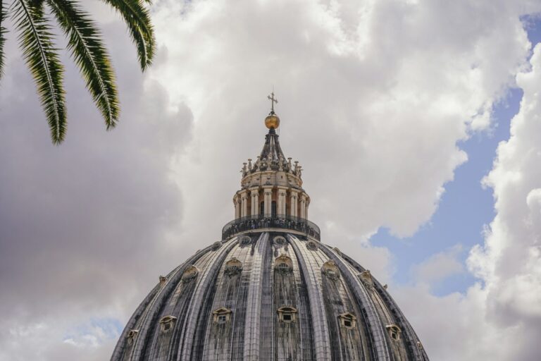 The dome of St. Peter’s Basilica rising against a blue sky, seen from the Vatican Gardens.