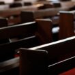 Rows of empty wooden pews inside a Catholic church.