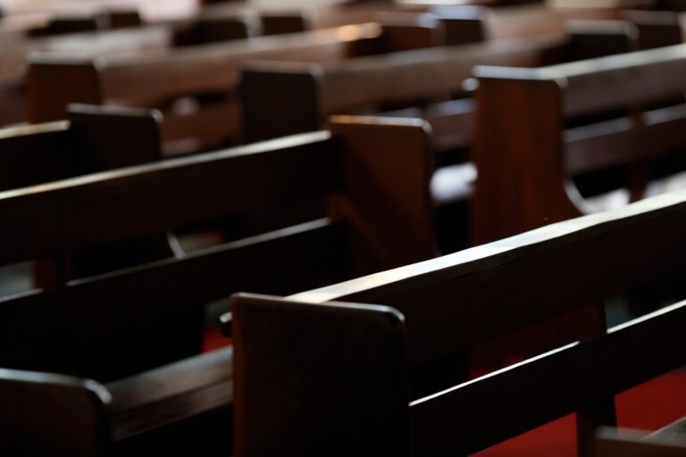 Rows of empty wooden pews inside a Catholic church.