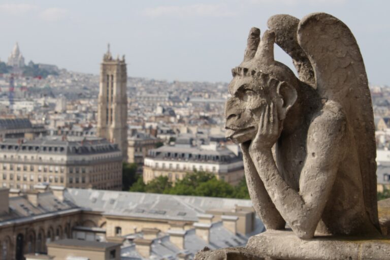 Stone chimera of Notre-Dame de Paris resting its chin in its hand, gazing over the Paris rooftops and the Tour Saint-Jacques