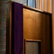 A purple priest’s stole hanging over a wooden confessional booth with a latticed window.