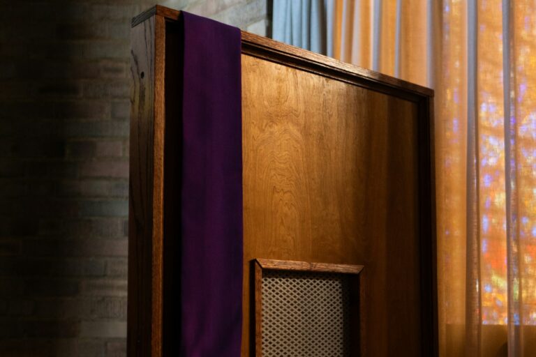A purple priest’s stole hanging over a wooden confessional booth with a latticed window.