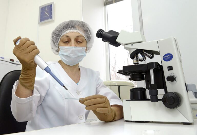 Laboratory technician working at a microscope and pipette in an IVF lab