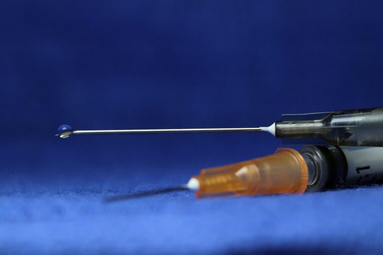 A syringe with a droplet of liquid at the tip of the needle.