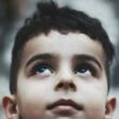 A young boy gazing up toward the sky with a hopeful expression.