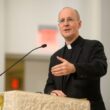 Fr. James Martin, S.J., in clerical collar, speaking at an ambo with a microphone.