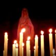 Statue of the Virgin Mary praying behind rows of lit votive candles