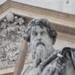 Statue of St. Paul with his sword in front of the carved stone facade of St. Peter’s Basilica in Rome.